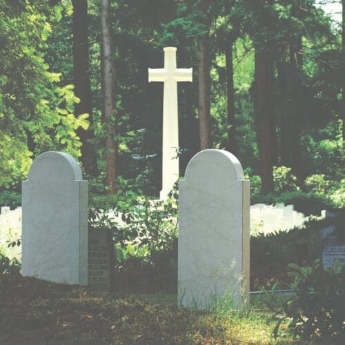 Peaceful cemetery scene with gravestones and cross amidst lush trees, evoking a sense of tranquility and reflection.