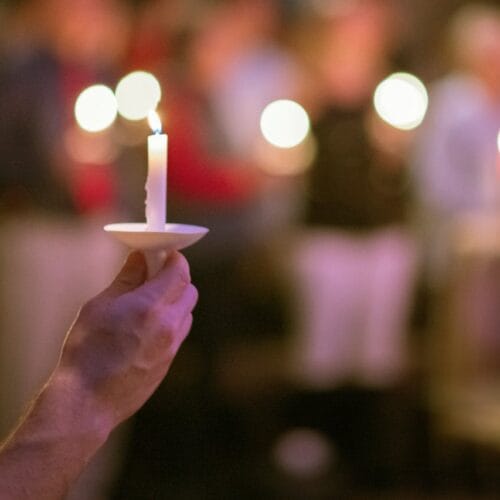 A serene scene of a hand holding a candle during a candlelight vigil, with blurred background.